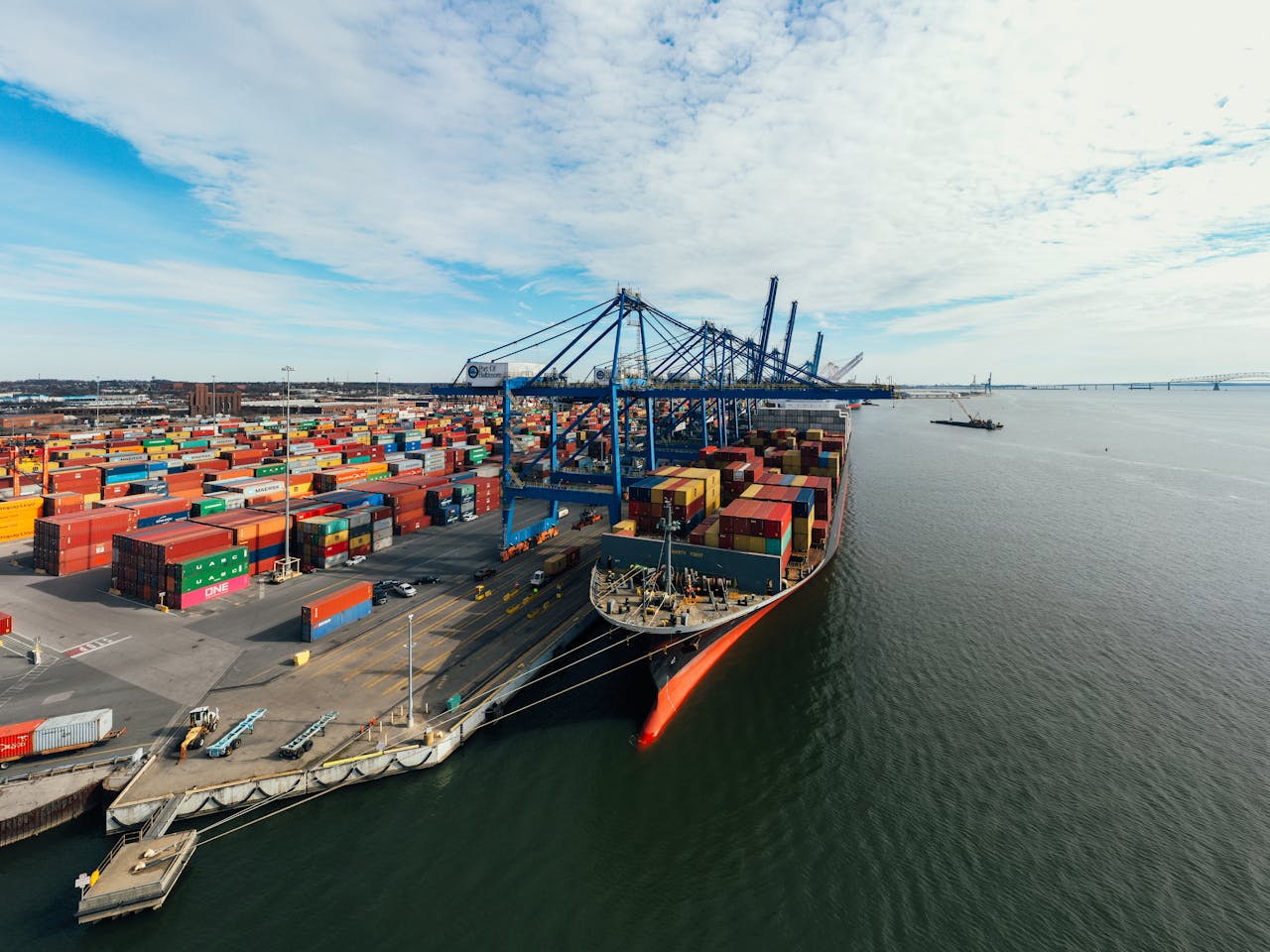 Aerial view of Baltimore cargo port with colorful shipping containers and cranes along the waterfront.